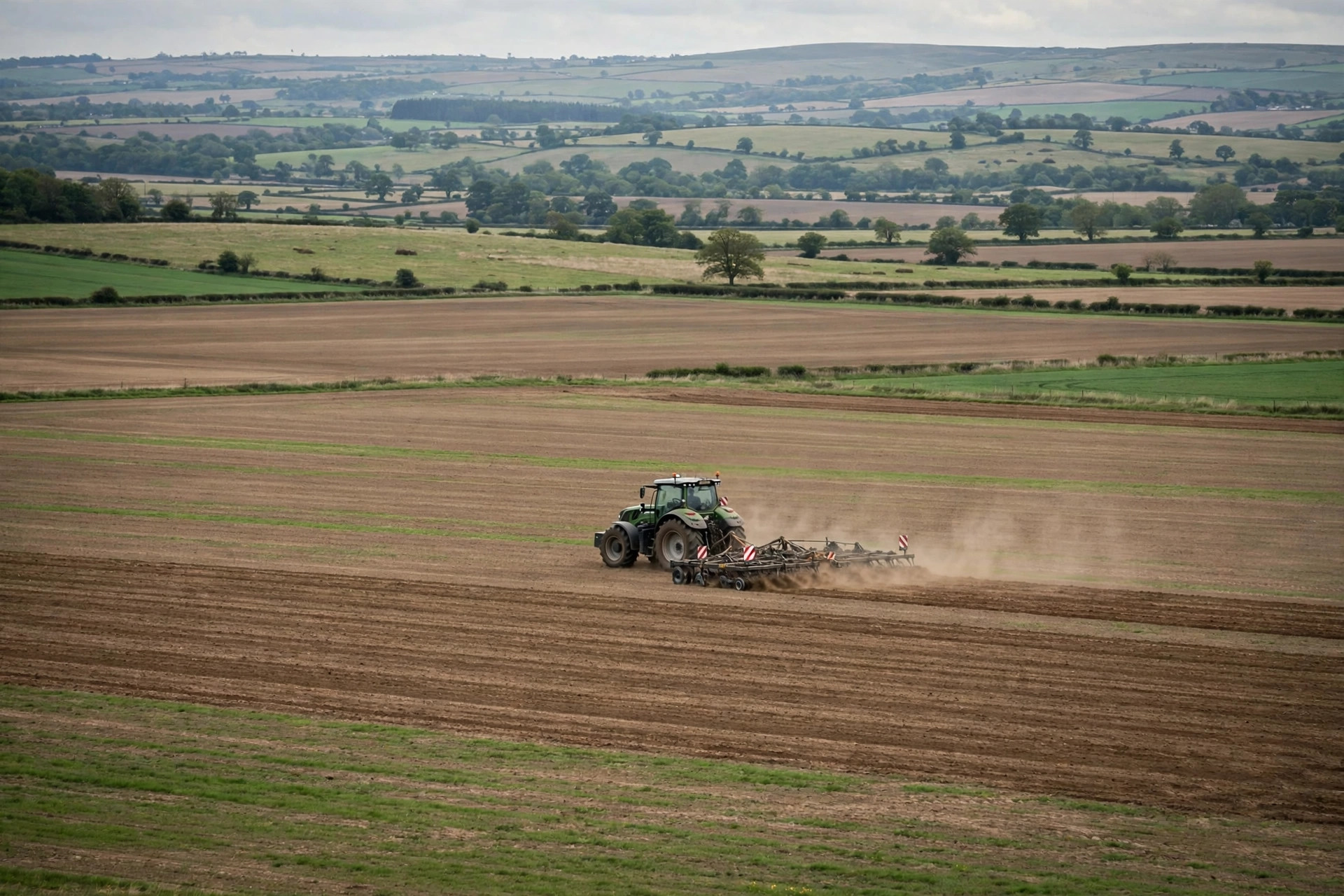 A tractor with farming implements working in a field, viewed from a distance